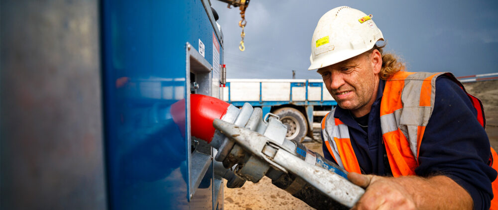 Medewerker met helm plugt slang aan op machine